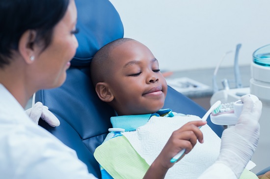Child in dental chair brushing tooth model.