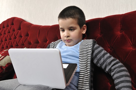 Child sitting on couch looking at laptop on lap.