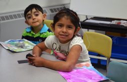 Young girl and both with hearing aids sitting and smiling in a classroom.