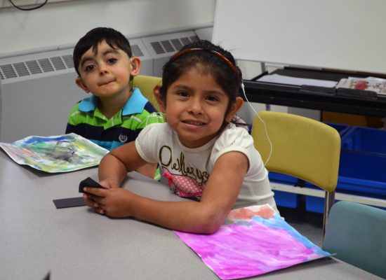 Young girl and both with hearing aids sitting and smiling in a classroom.