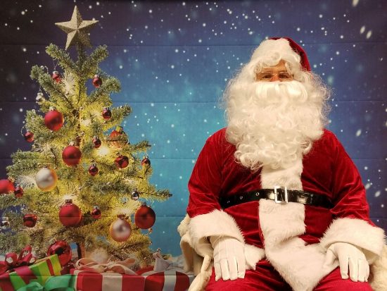 Santa Claus poses in front of a Christmas tree backdrop at the DSCC Mokena Regional Office.