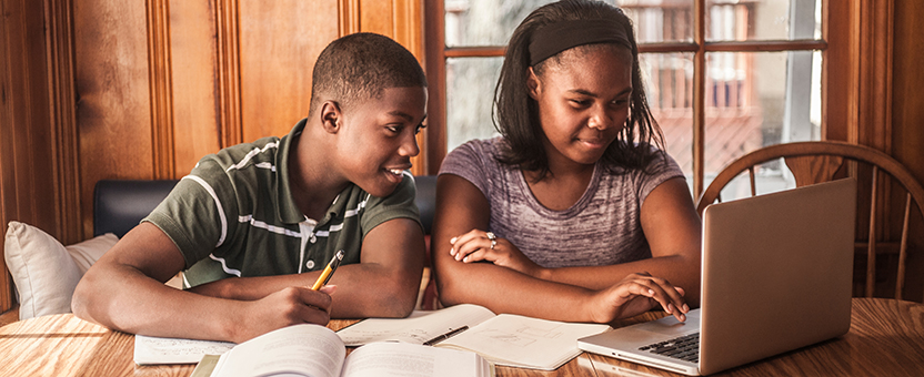 Young man and young woman look at a laptop while taking notes