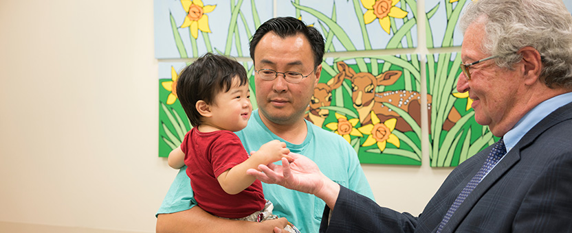 Young boy shakes physician's hand while in his father's arms