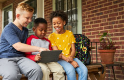 Three kids looking at a laptop together while sitting on a porch