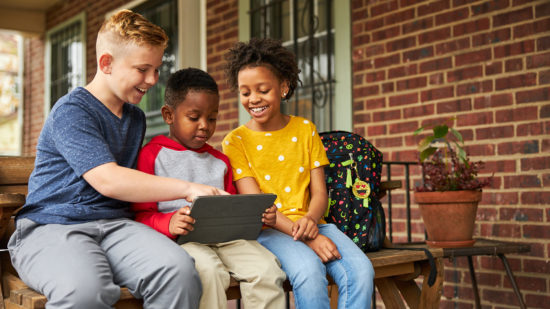 Three kids looking at a laptop together while sitting on a porch