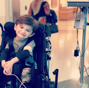 Nash Stieman smiles as he sits in his wheelchair and is hooked up to an IV.