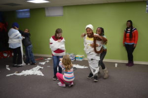 Club Compass students and DSCC staff laugh as they wrap each other in toilet paper to build a "snowman" 