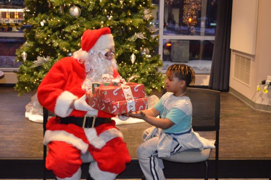 Santa gives a stack of gifts from DSCC staff to an eager Club Compass student.