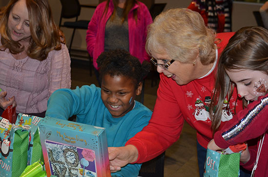 A Club Compass student smiles as she opens a Christmas present donated by Division of Specialized Care for Children Staff