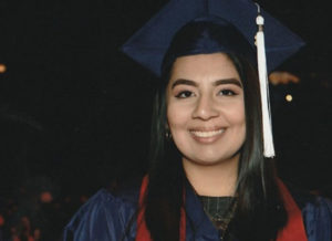 DSCC former participant and current employee Lisette Rios smiles while wearing her graduation cap and gown.