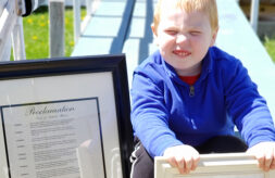 Eldon smiles while holding a framed copy of his city's Apraxia Awareness Day proclamation