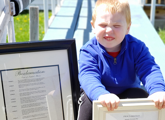 Eldon smiles while holding a framed copy of his city's Apraxia Awareness Day proclamation