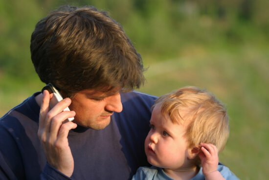 A young son mimics his father who is talking on his mobile