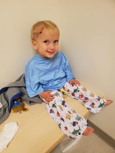 Ryker, wearing a hospital gown and pants, smiles before having an MRI