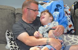 A medically complex little boy smiles up at his father while sitting in his arms