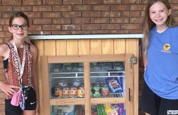 Emma Wiker and her sister, Ellen, stand on either side of a community pet pantry they opened in Athens, Ill.