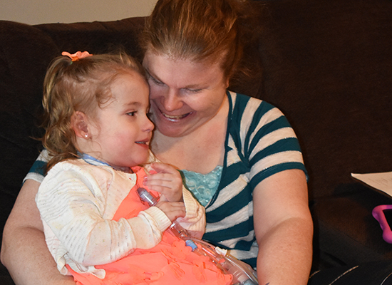 A mom holds her young daughter with complex medical needs and smiles at her
