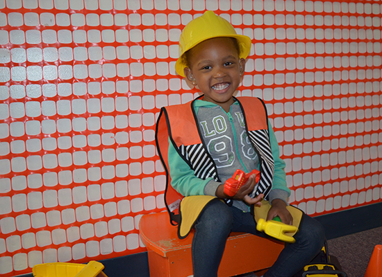 A young girl with hearing aids smiles while dressed up as a construction worker