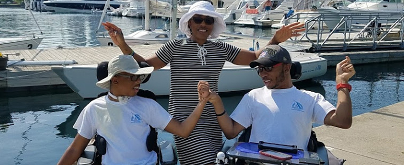 Two teenaged brothers with medical complexity clasp hands while posing with their mother in front of sailboats