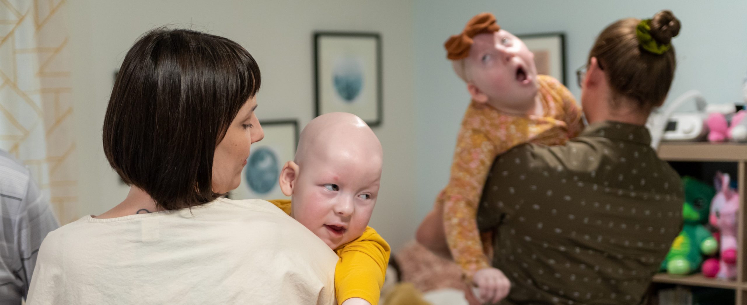 Erica Stearns holds her son, Caratacus, who has complex medical needs. Erica's husband holds their daughter, Margot, who also has complex needs, in the background.