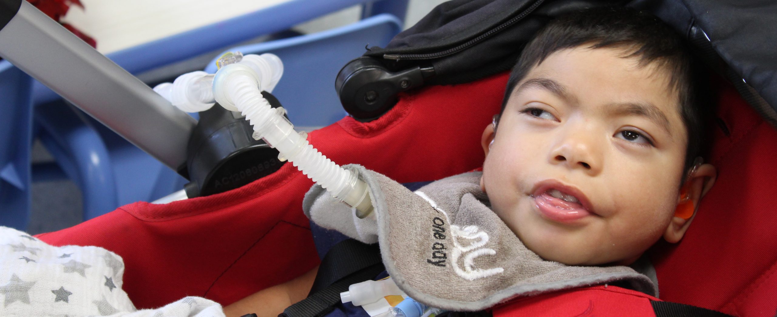 A young boy with a tracheostomy tube sits back in his stroller