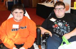 brothers Jaysen, 18, and Justen, 14, McMenamin smile as they sit in their power wheelchairs while attending the 2022 Illinois Statewide Transition Conference