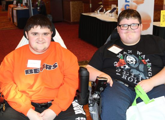 brothers Jaysen, 18, and Justen, 14, McMenamin smile as they sit in their power wheelchairs while attending the 2022 Illinois Statewide Transition Conference