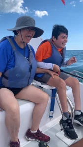 Daniel Barraza and his mom, Anita, hold hands and laugh while wearing life jackets and sitting on a boat that's moving through the water