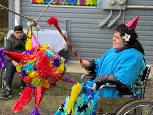 Diana Barraza wears a birthday party hat while swinging at a brightly colored pinata while sitting in her wheelchair