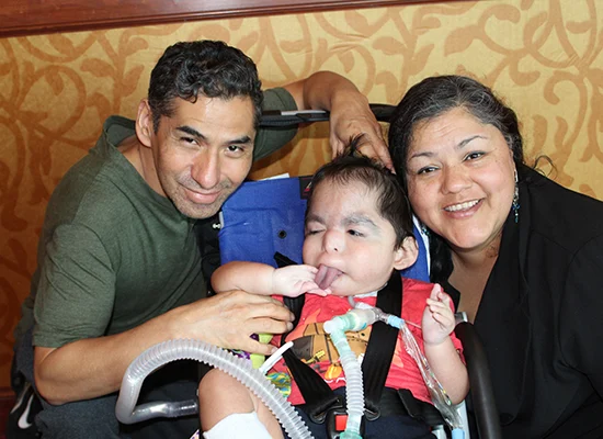 Jacob Ortiz, a young Hispanic boy with a tracheostomy, sits in his stroller between his two parents