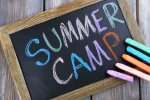 The text, "Summer Camp," written with chalk on chalkboard next to chalk sticks of different bright colors