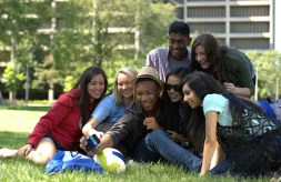 diverse group of college students taking a selfie in a grassy area outdoors on a college campus