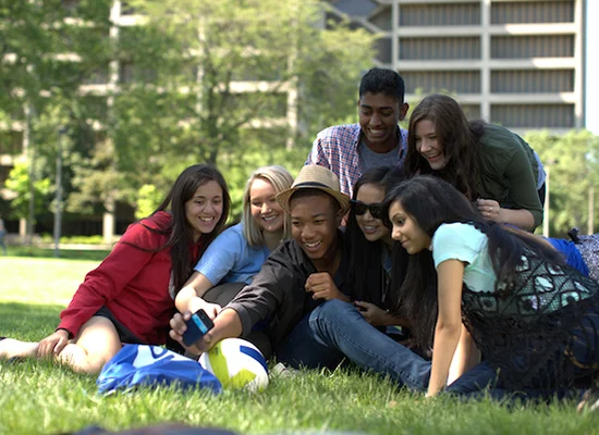 diverse group of college students taking a selfie in a grassy area outdoors on a college campus