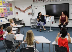 The Institute's school-age children sit at desks inside a classroom at the Illinois School for the Deaf and sign along as a teacher reads a story in American Sign Language