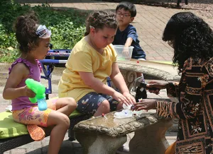 Institute participants Dream, Nevaeh and Freddy participate in an ice sensory activity outdoors with Illinois School for the Deaf Cadet Shavon.