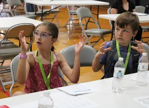 A girl and boy whose younger sibling has hearing loss learn sign language during the Institute. 