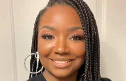 Meeka Harris earns the 2024 DSCC Award of Merit. She has long, dark hair that is parted at the side and braided in many narrow braids, She has light brown skin, a beautiful smile and brown eyes, She is wearing a grey t-shirt and silver hoop earrings.