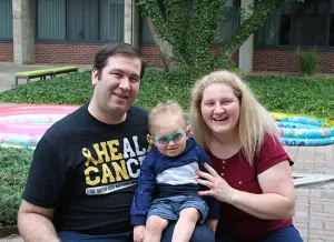 Parents Aaron and Basia hold their son Christian between them and smile while in the courtyard on the Illinois School for the Deaf campus. Christian is a toddler with hearing loss.