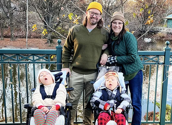 Erica Stearns and her husband stand arm-in-arm between their children Margot and Caratacus Stearns who are in medical wheelchairs while the family enjoys time outdoors