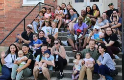 A group of 12 families who attended the 2024 Institute for Parents of Preschool Children Who Are Deaf or Hard of Hearing pose together on the steps of the dorms on the Illinois School for the Deaf campus.