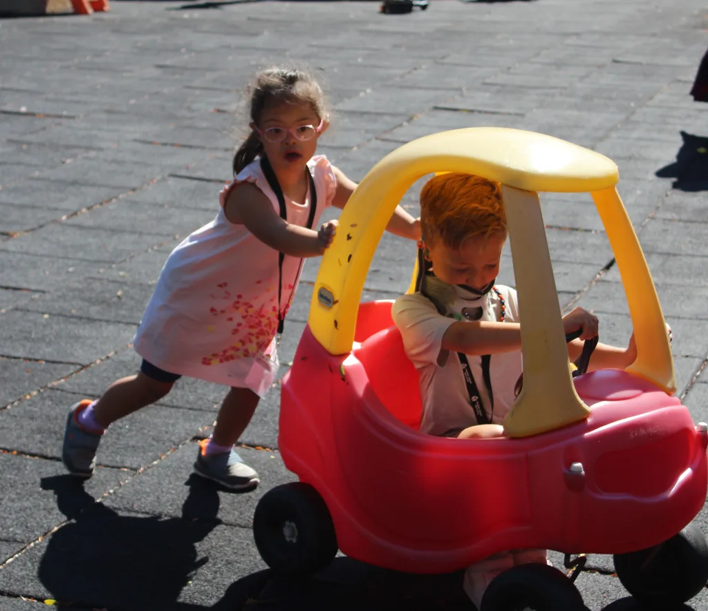 Institute participant Kimberly pushes a red toy car as her classmate Luke drives it around the playground.