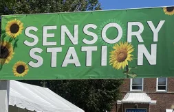 The green Sensory Station banner that's decorated with sunflowers and posted outside the entrance to the Sensory Station building on the Illinois State Fair fairgrounds
