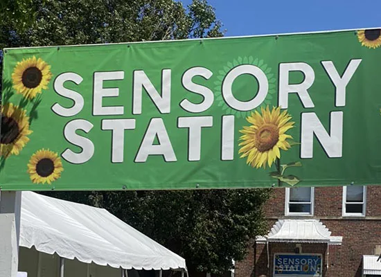 The green Sensory Station banner that's decorated with sunflowers and posted outside the entrance to the Sensory Station building on the Illinois State Fair fairgrounds