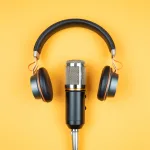 A set of headphones resting above a recording microphone on an orange background