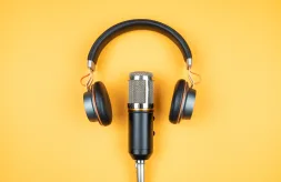 A set of headphones resting above a recording microphone on an orange background