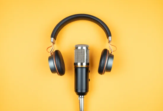 A set of headphones resting above a recording microphone on an orange background