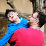 A father holds and plays with his son with disabilities while enjoying time together outdoors.