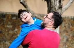 A father holds and plays with his son with disabilities while enjoying time together outdoors.