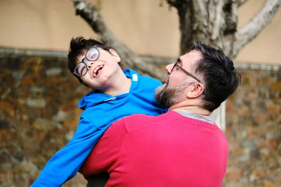 A father holds and plays with his son with disabilities while enjoying time together outdoors.