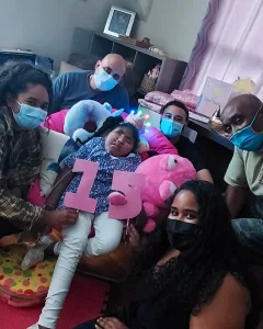 DSCC participant Davina wears a ligh-up pink crown and holds large pink numerals "1" and "5" while surrounded by her family members wearing masks on her 15th birthday 